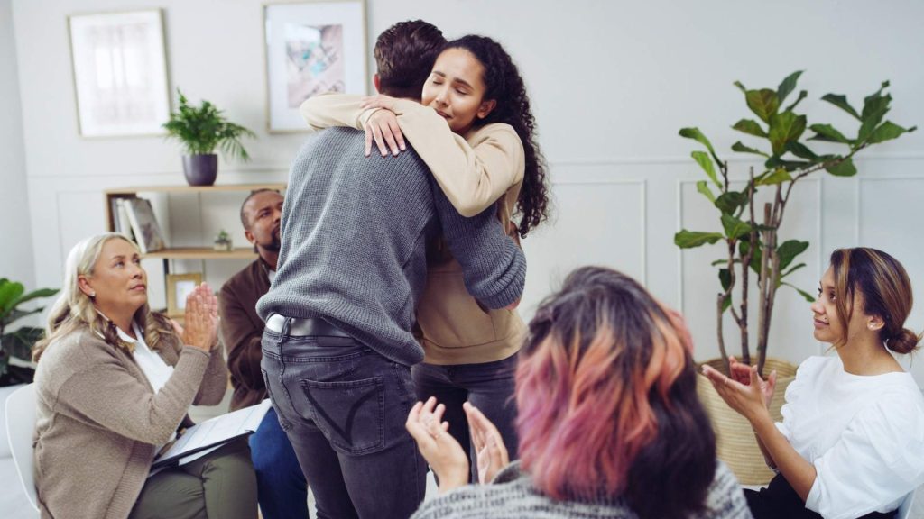 People embracing during group therapy for addiction while others offer support